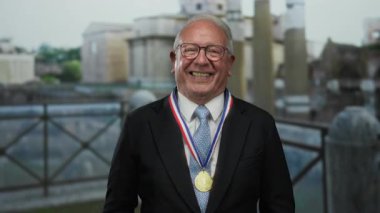 Takım elbiseli yaşlı adam, boynunda altın bir madalyayla gururla dışarıda gülümsüyor. Tarihi Roma harabelerinin ortasında, eşsiz bir başarı ve neşe anı yakalıyor..