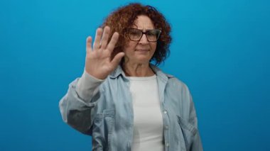 Kot pantolonlu kadın, ciddi ifadesini ve günlük kıyafetlerini vurgulayan canlı mavi bir duvara el kaldırıyor..