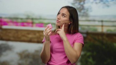 Pembe tişört giyen kadın, üzerinde dalgın bir ifade olan regl fincanı tutuyor. Bulanık doğal arka plan, gündelik ortamlarda kadın sağlığının farkında olduğunu gösteriyor..