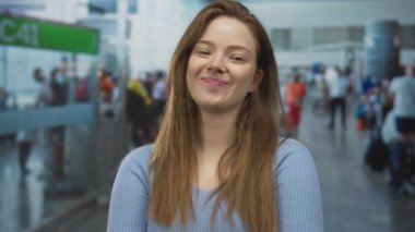 Mavi kazaklı kadın havaalanı terminalindeki gezgin kalabalığın arasında başını eğiyor ve dilini dışarı çıkarıyor; neşeli ruh hali.