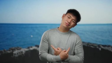 Sahil kenarında sakin bir sahilde, temiz gökyüzünün altında düşünceli bir ifadeyle poz veren genç adam..