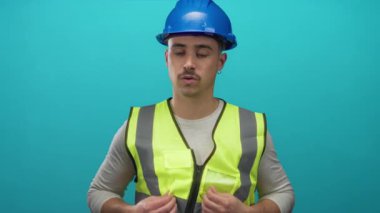 Şapkalı genç İspanyol adam mavi duvara karşı yansıtıcı yelek giyiyor..