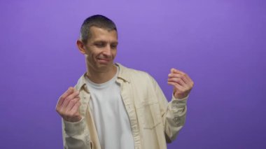 İzole edilmiş mor arkaplan karşısında el kol hareketi yapan, günlük beyaz gömlek giyen ve duygulara ve eyleme odaklanmış oyuncu bir şekilde gülümseyen bir adam..