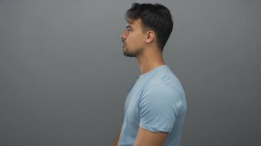 Açık mavi tişörtlü İspanyol genç adam gri bir arka plana karşı poz veriyor. Tarafsız ve ön profilli bir ifade sergiliyor..