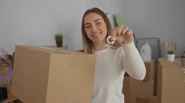 Anahtarları elinde tutan ve evin içinde kutu taşıyan kadın, parlak iç mekanda yeni evi kutlayan kadın, taşınma ve ev sahipliğinin sevincini sembolize ediyor..