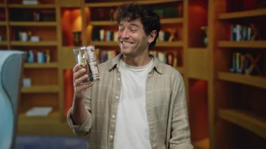 Bir kütüphanede elinde domuz kumbarası olan İspanyol bir adam güvenle gülümsüyor ve biz dolarları görünür kılıyor..