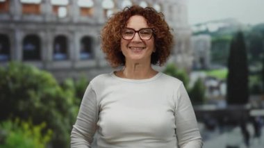 İkonik Roma Kolezyumu 'nun yakınındaki hashtag' i işaret eden kadın kıvırcık esmer saçlar ve neşeli bir ifade sergiliyor, İspanyol özelliklerini ve şehir dışını vurguluyor..