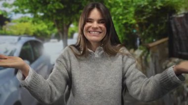 Şehir merkezinde ağaçların arasında gülümseyen Latin kökenli genç bir kadın park halindeki arabanın yakınındaki kameraya öpücük yollarken mutlu bir ifade sergiliyor.