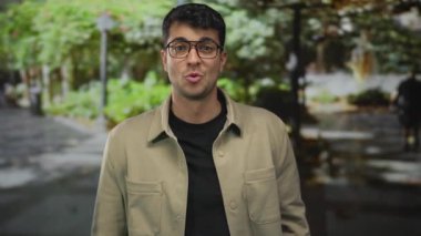 Genç Latin asıllı bir adam sokakta ağzını açık gösteriyor. Gözlüklü bir adam, bilinmeyen bir olayı fark ediyor..