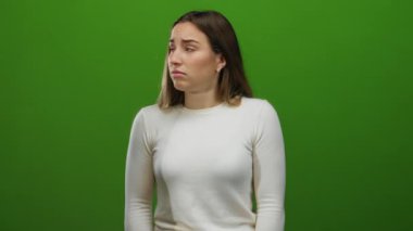 Yeşil arka planda şaşırmış bir kadın, izole edilmiş ortamı vurgulayan boş bir duvarla şok ve duygu tasvir ediyor..