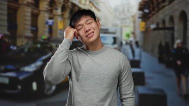 Gri kazaklı genç Çinli adamın taksilerle ve arka planda insanlarla dolu bir caddede parlak bir fikri var..