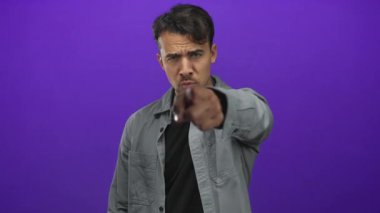 İzole edilmiş mor arka planda kameraya el sallayan İspanyol genç adam buraya ciddi bir ifadeyle geldiğini ve odaklandığını gösteriyor..