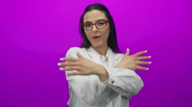 Gözlüklü ve beyaz tişörtlü İspanyol bir kadın canlı pembe bir duvara sarılıyor. Renkli ve neşelendirici bir ortamda neşe ve güveni ifade ediyor..