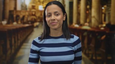 Kilisede sessiz kalan bir kadın çizgili bir süveter giyiyor. Genç İspanyol bir yetişkin. Etrafında sütunlar ve banklar olan dini bir ortamda..