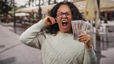 Açık hava restoranında elinde Mısır banknotları olan orta yaşlı bir kadın teras geçmişiyle enerjik bir şekilde bağırıyor heyecan ve finansal başarıyı temsil ediyor..