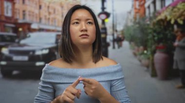 İşlek bir şehir caddesinde parmakları olan, arka planda arabaları ve yayaları olan, mavi bluzlu, açık hava ortamında düşüncelerini ifade eden bir kadın..