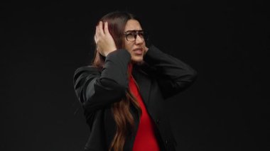 Gözlüklü genç bir kadın, izole edilmiş siyah arka plan yüzünden stresli, resmi giyinmiş, hayal kırıklığını ve kaygıyı anlamlı bir şekilde gösteriyor..