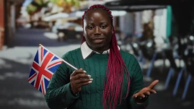 Teras restoranının caddesinde İngiliz bayrağı tutan kadın, Afrika ve İngiliz kültürlerini harmanlayan şehir atmosferini resmediyor..