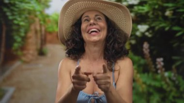 Güneşli parkta, açık havada şapkasıyla gülümseyen bikinili bir kadın yeşil ve canlı doğayla çevrili, bereketli manzaralı bir ortamda neşeli yaz titreşimleri sergiliyor..