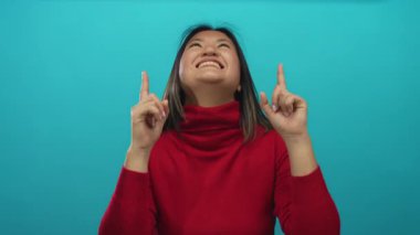 Kırmızı kazaklı kadın mavi arka planı işaret ederek gülümsüyor. Mutluluk ve pozitifliği güvenli bir şekilde aktarıyor..