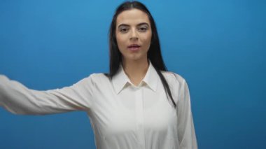 Beyaz tişörtlü İspanyol kadın gözlerini eliyle kapatıyor. Mavi duvarlı arka plandaki ifadeyi ortaya çıkarıyor..