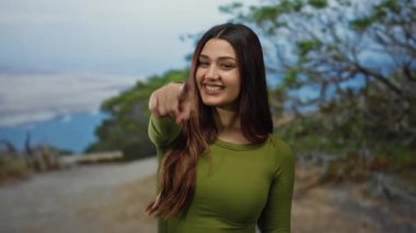 Arka planda yeşillik, neşe ve bağın somutlaştığı manzaralı açık hava parkında gülümseyen ve yeşil tişörtlü İspanyol kadın..