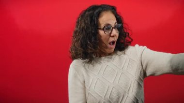 Kıvırcık saçlı İspanyol kadın canlı kırmızı duvara ip çekerek dinamik ifade ve enerji gösterisi yapıyor..