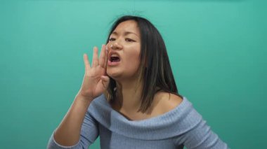 Sıradan kıyafetlerle izole edilmiş yeşil arka planda bağıran bir kadın, net bir şekilde yüzüne odaklanmış duygularını ifade ediyor, modern iletişimi resmediyor..