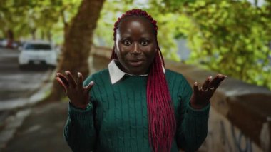 Pembe örgülü bir kadın, yeşil bir süveter içinde ağaçlar ve arabalarla dolu yemyeşil bir parkta dikilirken şaşkınlığını dile getiriyor..