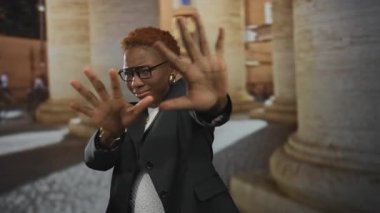 Genç Afrikalı Amerikalı kadın, eski köşe yazıları olan bir caddede ellerini kameraya doğru itiyor..