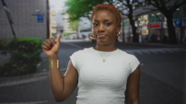 Şehir binaları arasında beyaz kolsuz bluz giyen ve parmakla işaret eden kadın..