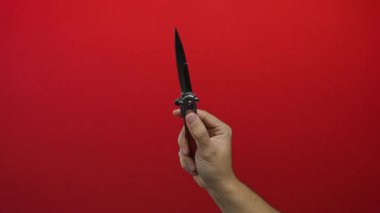 Kırmızı arka planda bıçak tutan bir adam izole edilmiş bir elle keskin bir bıçak ve dramatik bir kontrast yakalıyor..