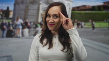 Genç İspanyol kadın Pisa 'daki meydanın yakınındaki tapınağına parmaklarıyla selam veriyor; seyahat neşesini selamlıyor.