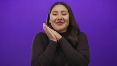 Stüdyo ortamında gülümseyen ve elleri çene jestinin altına sıkışmış, gözleri kapalı genç İspanyol bir kadın..