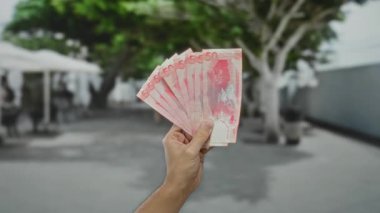 Pembe banknotlar sergilenen bir şehir caddesinde el ele tutuşan Filipinli pesolar, sahnenin odak noktası bir adamın elinde tuttuğu para..