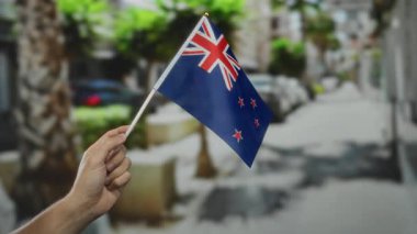 Şehir sokağında yeni Zelanda bayrağını tutan el ele tutuşmuş, ağaçlar gün ışığı altında açık havada gururlarını sergiliyor.