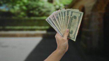 Amerika Birleşik Devletleri 'nin dolarlarını elinde tutan beyaz bir adam yeşil bulanık bir arka planla servetini ve finansal başarısını gösteren bir şehir caddesinde açık hava banknotları tutuyor..