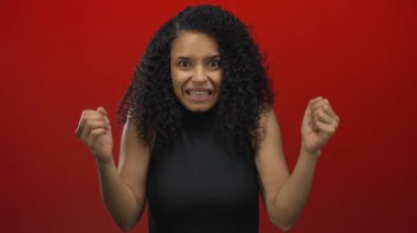 Kıvırcık saçlı, cesur kırmızı arka plana karşı şaşırmış bir kadın dramatik bir duygu ve yoğunluk sahnesi yaratıyor. Ham ifadesini ve soyutlanmış varlığını sergiliyor..