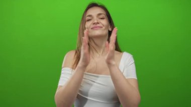 Beyaz omuzlu kadın, stüdyoda ellerini birbirine kenetledi. Arkaplanda yeşil bir perde vardı..