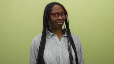 Örgülü ve gözlüklü bir kadın sarı arka plana şüpheyle bakıyor, çizgili bir gömlek giyiyor, merakını iletiyor ve bakışlarını sorguluyor..