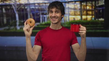 Sokak lambalarının altında kırmızı tişörtlü, elinde çörek ve kupa tutan bir adam. Mutluluk..