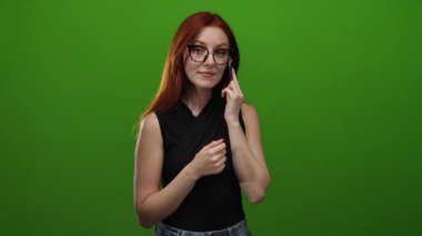 Telefonda konuşan kızıl saçlı kadın yeşil duvara karşı şşşş hareketi yapıyor, yetişkin kadın iletişimi gösteriyor..