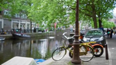 Amsterdam Kanalı 'nın bulanık manzarası. Odaklanmış bisikletler ve yeşillik sakin suya yansıyor. Şehir yaşamını yakalıyor..