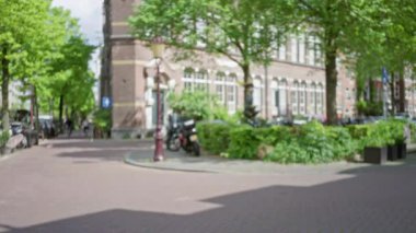 Ağaçlar, binalar ve yürüyen bir adam, güneşli bir günde sakin bir açık hava ortamı yaratarak arka plandaki bokeh etkisini artırıyor..