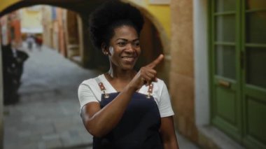 Önlük takan bir kadın canlı bir şehir caddesinde dikilirken, açık hava yaşamını yansıtıyor..