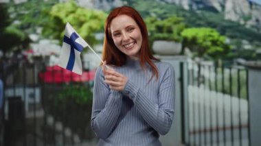 Elinde Finlandiya bayrağı olan bir kadın şehrin dışında finniş gururunu kızıl saçlı ve neşeli bir ifadeyle sergiliyor.