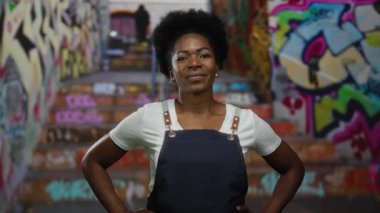 Önlük giyen kadın, duvar yazısıyla kaplı şehir merdivenlerinde kendinden emin bir şekilde duruyor. Kentli, genç ve canlı bir atmosfer yayıyor..