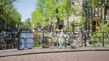Amsterdam Kanalı 'nın orada ağaçlarla ve arka planda büyüleyici evlerle park etmiş bisikletlerin odaklanmamış görüntüsü huzurlu seyahat görüntüleri için mükemmel, bulanık bir şehir atmosferi yaratıyor..
