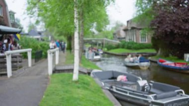 İnsanlarla, ağaçlarla, köprülerle dolu giethoorn kanalındaki teknelerin bulanık görüntüsü. Titrek bir gökyüzü altında sakin bir Hollanda köyü atmosferinin özünü yakalıyor..