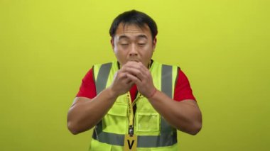 Yelek giyen genç adam sarı arka planda el ele tutuşurken şaşırdı.